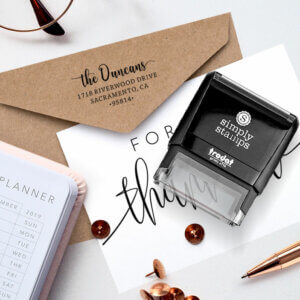 Self-inking address stamp laying on envelope next to a planner and elegant pen